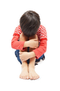 Sad little boy sitting face down on knees on white background